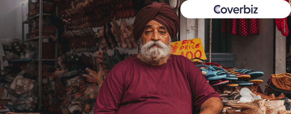 an Indian shopkeeper in his middle age sitting infront of his shoe shop