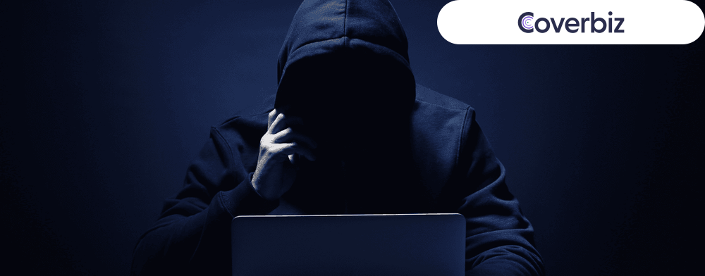 a person wearing a dark hoodie sitting infront of his laptop in a dark isolated place