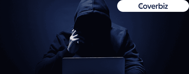 a person wearing a dark hoodie sitting infront of his laptop in a dark isolated place